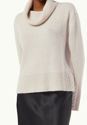 Kvinde iført en lys pink chunky strikket rullekrave, kombineret med en sort satin nederdel, overkrop og arme synlige.