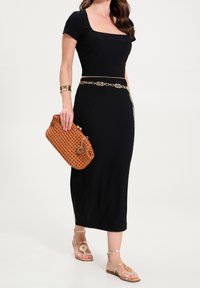 Czarna, prążkowana sukienka midi z krótkimi rękawami i prostokątnym dekoltem, uzupełniona złotym paskiem łańcuszkowym i pomarańczową plecioną kopertówką.