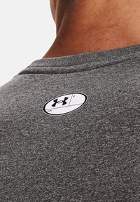 Grå trenings t-skjorte med rund hals. Har et hvitt merkelapp med logo bak, som viser tekstur og sømdetaljer.