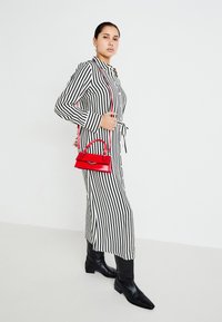 Pruhované čierno-biele dlhé šaty s golierom a viazaním v páse, doplnené malou červenou kabelkou a čiernymi koženými čižmami po kolená.