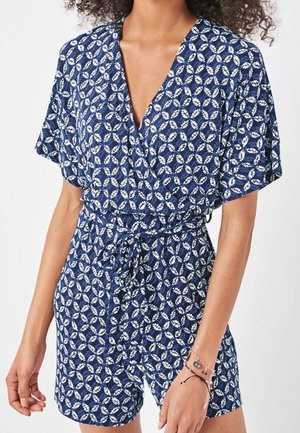 Combinaison bleu marine avec un design portefeuille, manches courtes et un motif floral blanc et vert. Présente une taille cintrée et un détail de nouage.