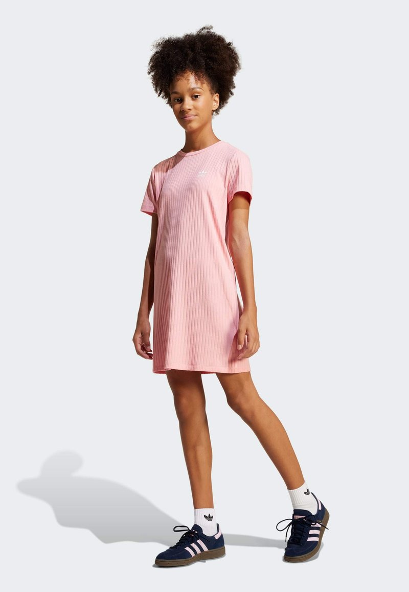 Rózsaszín bordázott ruha rövid ujjakkal, laza fazonnal és kerek nyakkivágással. Sötétkék sportcipővel és fekete logós fehér zoknival párosítva.