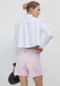 Weißes cropped Shirt mit rosa Akzenten an den Ärmeln, kombiniert mit hellrosa Shorts. Das Outfit zeichnet sich durch klare Linien und eine lockere Passform aus.
