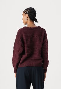 Maglione lavorato a maglia bordeaux con motivi testurizzati, vestibilità oversize, spalle cadenti e polsini e orlo a coste. Visualizzazione della parte posteriore.