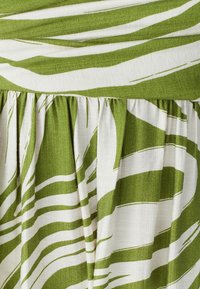 Grønt og hvidt stribet stof med en glat tekstur, der har et rynket design og elastisk taljebånd.