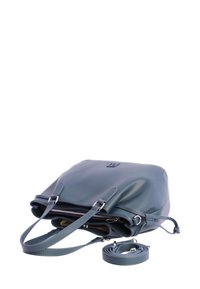 Bolso de piel en un verde azulado oscuro con asas dobles, apertura con cremallera y una correa de hombro enrollada y desmontable sobre un fondo blanco.