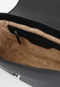 Svart läderväska med beige foder som har ett upprepat logomönster. Inkluderar en dragkedjeficka för organisering.