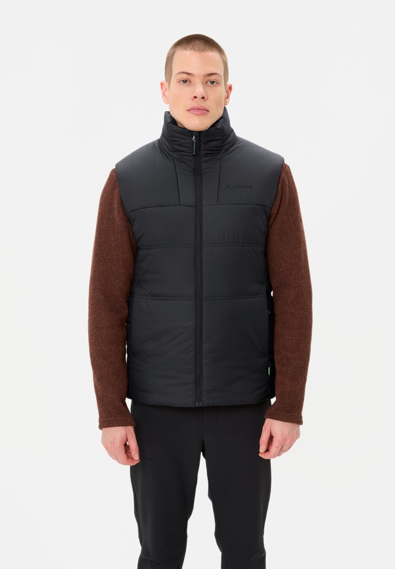 Schwarze ärmellose Steppweste mit hohem Kragen, gestepptem Design und Frontreißverschluss, kombiniert mit einem braunen Langarmshirt darunter.