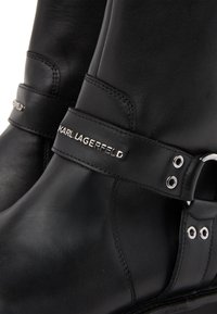 Μαύρες δερμάτινες μπότες με ραμμένες λουριά που διαθέτουν μεταλλικά τρουκς και ασημένιο λογότυπο Karl Lagerfeld στο λουράκι.