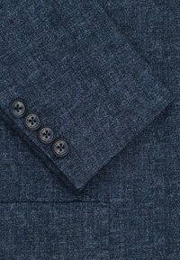 Rękaw marynarki w ciemnoniebieskim, teksturowanym materiale z czterema czarnymi guzikami oznaczonymi napisem "PAKO LONSKI".