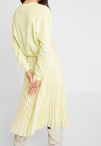 Gonna plissettata gialla chiara con una superficie testurizzata, abbinata a un maglione oversize abbinato. Il design presenta maniche lunghe e una vestibilità rilassata.