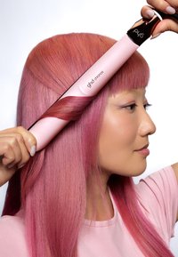 Hårstylingsverktyg i blushpink med en glänsande yta, som har en slät yta och en ergonomisk design, stylade hår i lösa vågor.