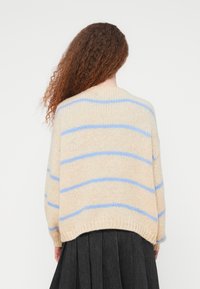 Π λεκτό πουλόβερ σε κρεμ χρώμα με γαλάζιες ρίγες· φαρδιά εφαρμογή, ριμπ μανσέτες και τελείωμα· απαλό ύφασμα, στρογγυλή λαιμόκοψη και χαμηλωμένοι ώμοι.