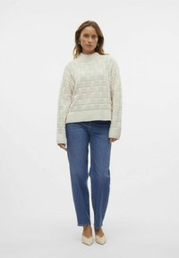 Chunky stickad tröja i krämfärg med strukturerad, vävd mönster; kombinerad med ljusblå raka jeans och beiga högklackade skor.