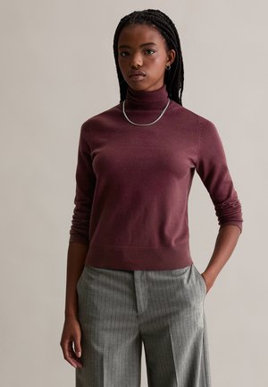 Bordeaux coltrui van een zachte tricot met geribde manchetten en zoom, gecombineerd met grijs gestreepte pantalons. Zilveren ketting als accent.