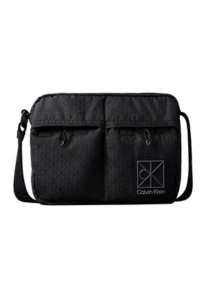 Sac bandoulière noir Calvin Klein avec sangle réglable, deux poches avant zippées, motif logo discret et patch logo Calvin Klein.