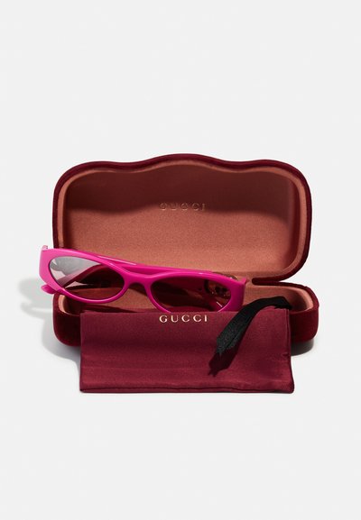 Růžové sluneční brýle Gucci s elegantním rámečkem uvnitř bordó sametového pouzdra, doplněné odpovídající utěrkou. Viditelné detaily zlatého loga.