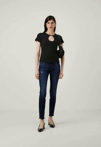 Μαύρο κοντομάνικο τοπ με κόψιμο σε σχήμα κλειδώματος, συνδυασμένο με σκούρες μπλε στενές τζιν και μαύρες γόβες με μυτερή μύτη. Μικρή μαύρη τσάντα ώμου προσθέτει έμφαση στην εμφάνιση.