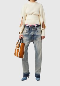 Suéter de punto acanalado en crema con mangas abiertas, vaqueros azul desgastado, bolso naranja con bordes de piel de oveja, y tacones azules de punta.