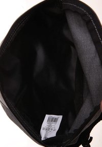 Pochette en tissu noir avec fermeture éclair, texture lisse et bords cousus. L'intérieur est doublé de matériau noir. Étiquette d'entretien visible.