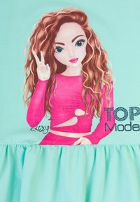 Abito verde menta con un'immagine di una ragazza con lunghi capelli castani ondulati, che indossa un top rosa con intagli e una gonna arricciata. Inclusa la scritta "TOP Model".