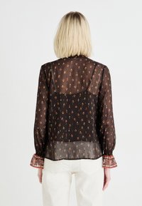 Blusa nera trasparente con motivo floreale, maniche lunghe, polsini elastici con decorazioni ricamate e pannello posteriore semitrasparente.