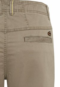 Beige broek met een textuurafwerking, voorzien van een achterzak en geborduurd logo. Gele stiksels accentueren de tailleband.