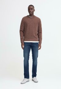 Rjav teksturiran pulover, okrogla izreza, v kombinaciji z modrimi denim hlačami in belimi športnimi copati. Preprost in sproščen slog oblačenja.