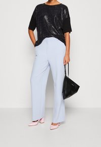 Černý top s flitry a krátkými rukávy, v kombinaci se světle modrými širokými kalhotami a růžovými lodičkami na podpatku. Drží černou kabelku.