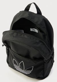 Črn najlonski nahrbtnik z glavnim žepom na zadrgo, sprednjim žepom in belim logotipom. Ima zgornji ročaj in nastavljive naramnice.