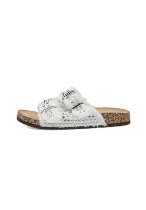 Sandalia blanca de denim tipo slide con tachuelas plateadas, dos hebillas ajustables, plantilla de corcho y suela de goma negra, mostrada de lado.