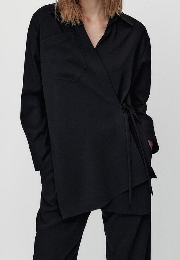 Mustat kietaisumallinen paita, jossa on pitkät hihat, kaulus, rintatasku ja vyötäröllä solmimisnauha. Valmistettu sileästä kankaasta, jossa on hieno kiilto.