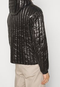 Quiltad svart dunjacka med en glänsande yta, med huva, elastiska muddar och horisontell vaddering för isolering.