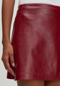 Roter Lederrock mit glatter Textur, A-Linien-Form und hoher Taille. Verfügt über einen subtilen Glanz und einen sauberen Saum.