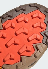 Η σόλα του παπουτσιού διαθέτει πορτοκαλί ελαστική βάση με υφή και έντονες καφέ προεξοχές πρόσφυσης, σχεδιασμένες για κράτημα και ανθεκτικότητα.