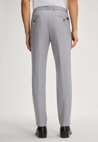 Pantaloni grigi chiari su misura con un tessuto strutturato, due tasche posteriori e un design slim fit, abbinati a scarpe nere.