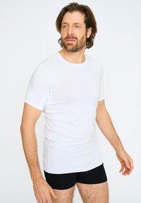 Hvid t-shirt med korte ærmer, lavet af glat stof, med rund halsudskæring og tætsiddende design, parret med sorte boxershorts.