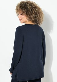 Marineblaue Strickjacke mit langen Ärmeln und Rundhalsausschnitt, mit seitlichen Schlitzdetails am Saum und strukturiertem Rippmuster an den Bündchen und am Halsausschnitt.
