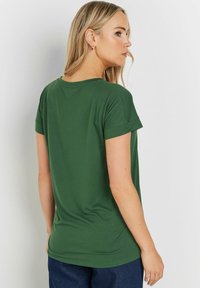 Grön kortärmad T-shirt i mjukt tyg, med en avslappnad passform och uppvikta ärmar, som har en slät textur och minimalistisk design.
