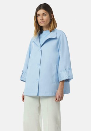 Lichtblauwe jas met een brede kraag, voorknopjes en manchetdetails met een subtiel patroon. Gekoppeld aan crèmekleurige broek met wijd uitlopende pijpen.