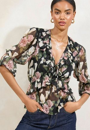 Blusa nera trasparente con motivo floreale in rosa e bianco, scollo arricciato, maniche corte e dettaglio con fiocco in vita.