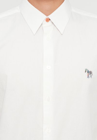 Camicia bianca a maniche lunghe, con colletto classico e un piccolo ricamo multicolore di un cavallo sul lato sinistro. Tessuto di cotone testurizzato.