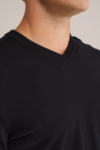 Črn pulover z V-izrezom, izdelan iz mehke tkanine. Ima gladko teksturo in prilegajočo zasnovo, ki poudarja dekolte in ramenski del.