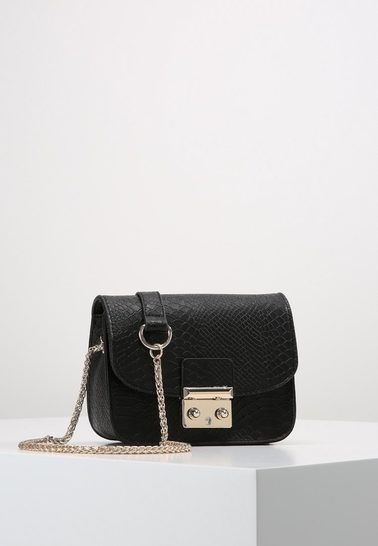 Czarna mała torebka na ramię z fakturowaną powierzchnią, srebrnym łańcuszkiem i prostokątną srebrną klamrą na białym postumencie.