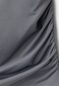 Tissu gris avec détail de fronces rassemblées sur un côté, montrant une texture lisse et des coutures fines.