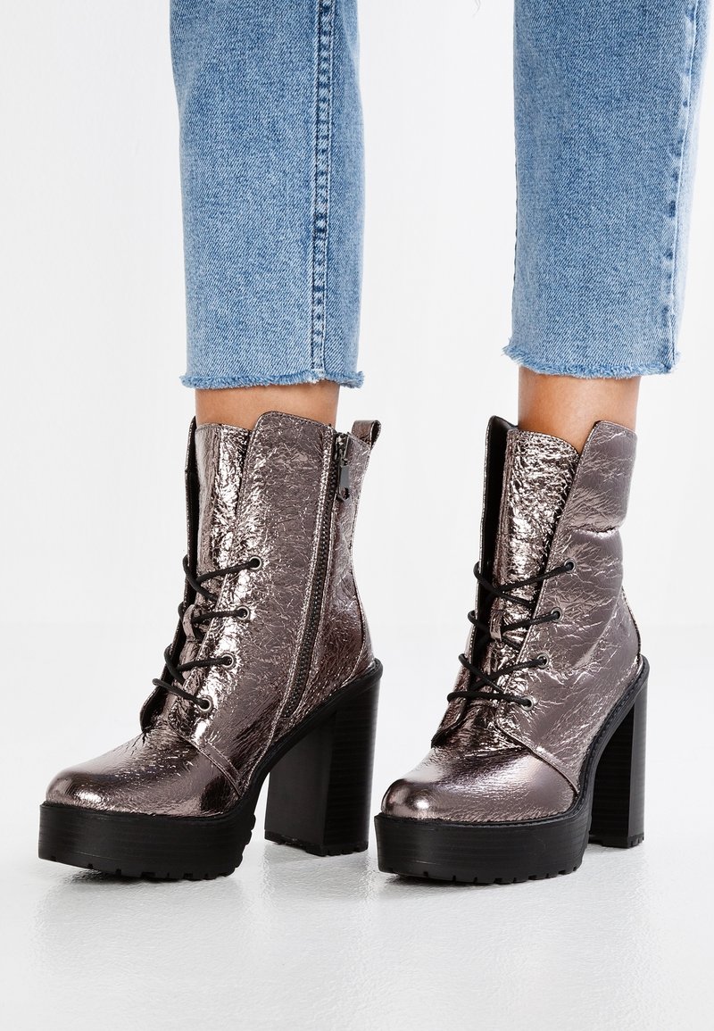 Bottes chevilles métalliques brillantes à talons hauts avec lacets noirs et semelles épaisses à plateforme, portées avec un jean court en denim bleu clair.
