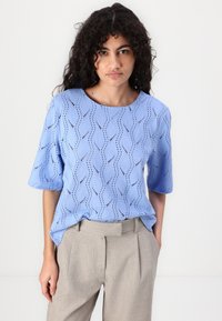 Lichtblauw perforated blouse met golvenpatroon, ronde halslijn en korte mouwen, gecombineerd met lichtgrijze hoge taille broek.