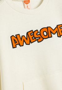 Ljusgrå sweatshirt med ribbad hals, med "AWESOME" i fet orange broderi. Inkluderar en framficka och mjuk textur.