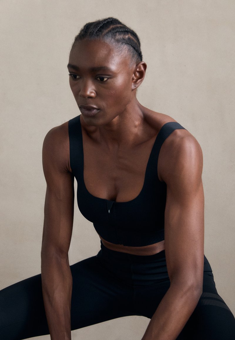 Melnas sporta krūšturis ar platām siksnām un priekšējo aizdari, kas izceļas ar gludu, viendabīgu audumu un pieguļošu dizainu, apvienots ar melnajām legingām.