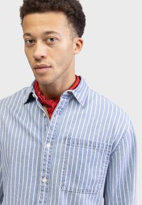 Blue and white striped button-up shirt with a pocket, made of denim-like fabric; red bandana around the neck adds color contrast.
